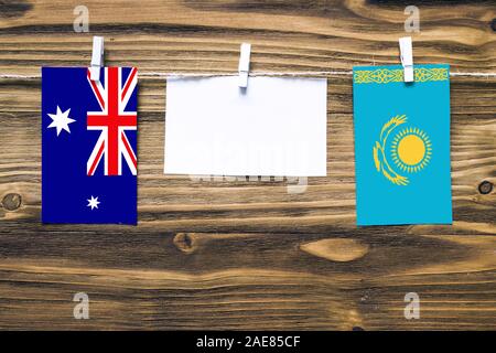 Hanging flags of Heard and Mcdonald Islands and Kazakhstan attached to rope with clothes pins with copy space on white note paper on wooden background Stock Photo