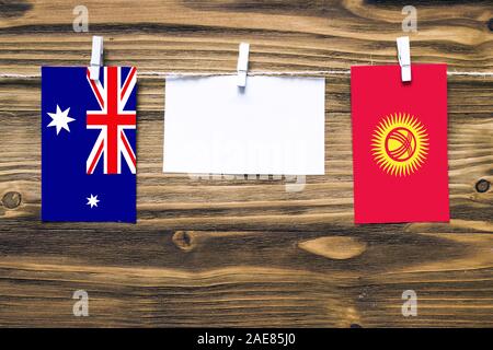 Hanging flags of Heard and Mcdonald Islands and Kyrgyzstan attached to rope with clothes pins with copy space on white note paper on wooden background Stock Photo