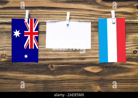 Hanging flags of Heard and Mcdonald Islands and Luxembourg attached to rope with clothes pins with copy space on white note paper on wooden background Stock Photo