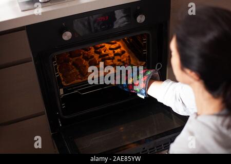 Woman pulls gingerbread out of the oven. Traditional Christmas gingerbread baking. Stock Photo