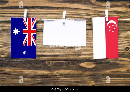 Hanging flags of Heard and Mcdonald Islands and Singapore attached to rope with clothes pins with copy space on white note paper on wooden background. Stock Photo