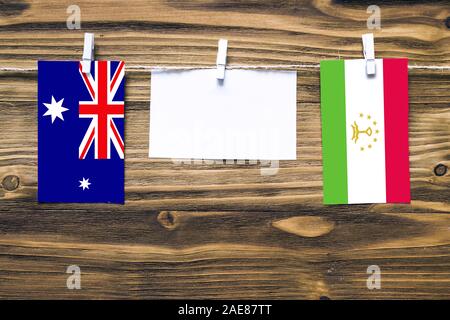 Hanging flags of Heard and Mcdonald Islands and Tajikistan attached to rope with clothes pins with copy space on white note paper on wooden background Stock Photo