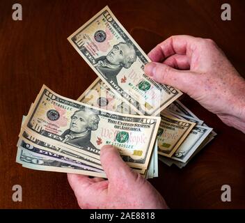 Man's hands counting American (US) money with five, ten & twenty dollar bills with US president Alexander Hamilton Stock Photo