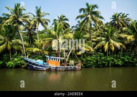 Old ocean fishing boat along the canal Kerala backwaters shore with palm trees at a sunny day between Alappuzha and Kollam, India Stock Photo