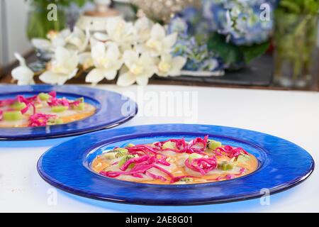 Front view of cod carpaccio with tomato cream, red cabbage, kiwi and roasted pine nuts on a blue plate over white background. Stock Photo