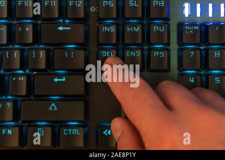 finger of a male hand presses the delete key on the backlit keyboard Stock Photo