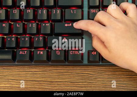 child finger presses enter on black keyboard with red backlight Stock Photo