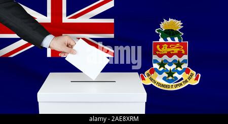 Election in Cayman Islands. The hand of man putting his vote in the ballot box. Waved Cayman Islands flag on background. Stock Photo