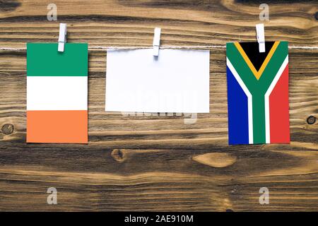 Hanging flags of Ireland and South Africa attached to rope with clothes pins with copy space on white note paper on wooden background.Diplomatic relat Stock Photo