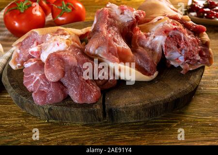 Homemade food preparation. Raw chopped pork knuckle оr leg and tomatoes lies on old dark wooden cutting board. Ready for cooking. Selective focus. Rus Stock Photo