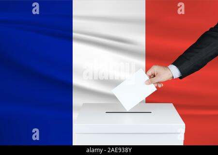 Election in France. The hand of man putting his vote in the ballot box. Waved France flag on background. Stock Photo