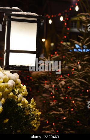 City metal lantern on a snowy winter night at Christmas and New Year eve with blurry festive lights of garlands in the background, copy space Stock Photo