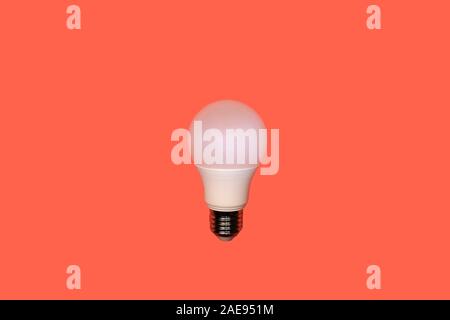 one white round type LED lamp with screw metal thread in the center on a red background, energy saving concept, copy space Stock Photo