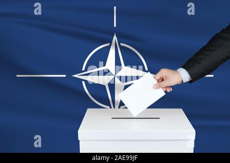 Election in North Atlantic Treaty Organization. The hand of man putting his vote in the ballot box. Waved North Atlantic Treaty Organization flag on b Stock Photo