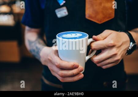 Male barista holding cup of blue matcha latte in hands Stock Photo