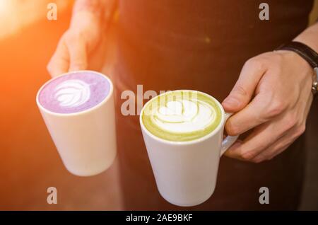 Male barista holding two cups of matcha latte in hands. Blue and green matcha, japanese drink Stock Photo