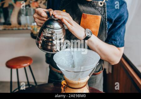 Hand pouring hot water from the kettle over the coffee powder. Male barista pouring boiling water from kettle Stock Photo