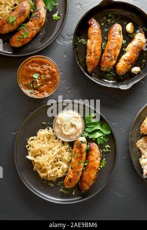 Grilled sausages with stewed sauerkraut and sauce over black stone background. Top view, flat lay Stock Photo