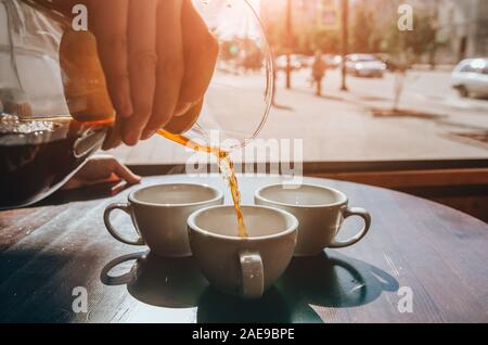 Barista pouring coffee into the ceramic white cup. Coffee shop terrace Stock Photo