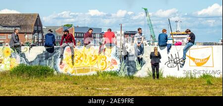 Woman talking to a group of young men sitting on a wall covered in graffiti drinking beers in the port of Cuxhaven Lower Saxony Germany. Stock Photo