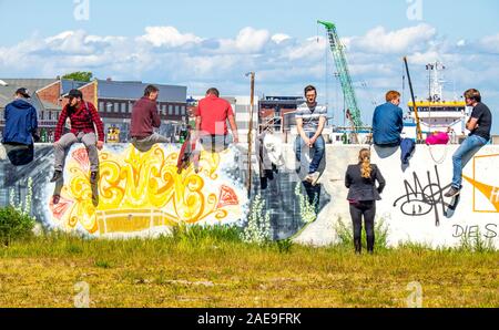 Woman talking to a group of young men sitting on a wall covered in graffiti drinking beers in the port of Cuxhaven Lower Saxony Germany. Stock Photo