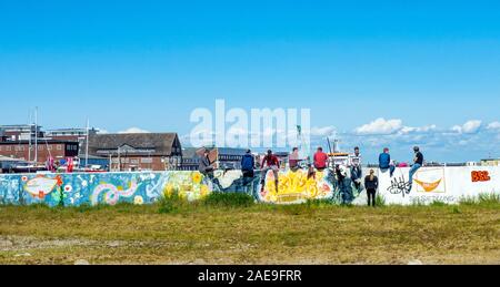 Woman talking to a group of young men sitting on a wall covered in graffiti drinking beers in the port of Cuxhaven Lower Saxony Germany. Stock Photo