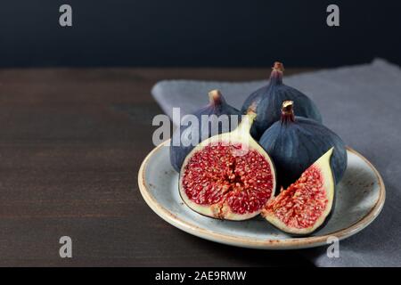 Fresh figs in a white plate on a dark background. Copy space. Purple ripe sliced and whole figs on a grey napkin. Side view. Stock Photo
