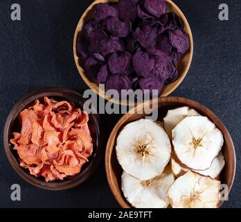 Dried carrot, beetroot and apple chips in a wooden bowl on a black stone background. Organic natural food. Top view, flat lay. Stock Photo