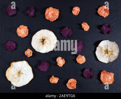 Dried carrot, beetroot and apple chips on a black stone background. Organic natural food. Top view, flat lay. Stock Photo
