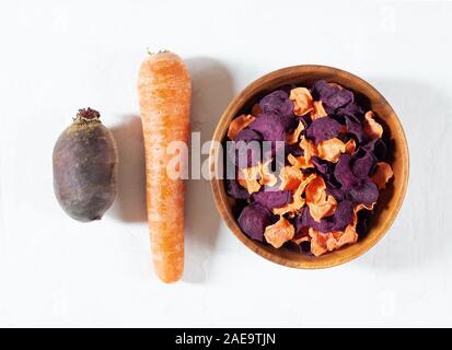 Dried carrot and beet chips in a wooden bowl and raw carrots, beets on a white concrete background. Organic natural food. Top view, flat lay. Stock Photo