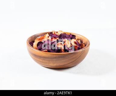 Dried carrot and beet chips in a wooden bowl on a white concrete background. Organic natural food. Side view. Stock Photo