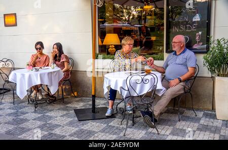 Caucasian couple and Asian couple sitting outdoor alfresco drinking alcoholic beverages at bar cafe in central Prague Czech republic. Stock Photo