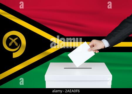 Election in Vanuatu. The hand of man putting his vote in the ballot box. Waved Vanuatu flag on background. Stock Photo