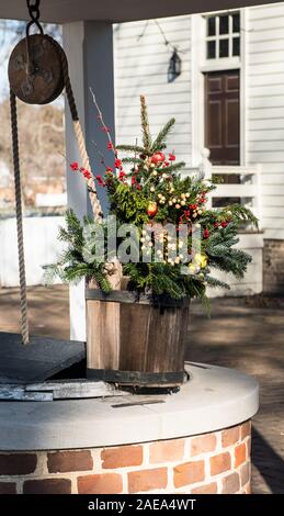 Dried wreath arrangement in a rustic wooden well bucket, Colonial Williamsburg. Red and green apples, pine cones, dried berries, evergreen branches, Stock Photo