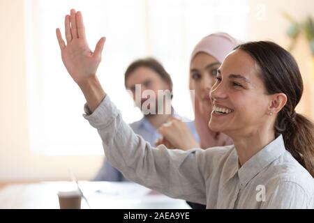 Happy mixed race female employee raising hand, asking question. Stock Photo