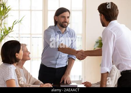 Smiling male boss shaking hands with young manager. Stock Photo
