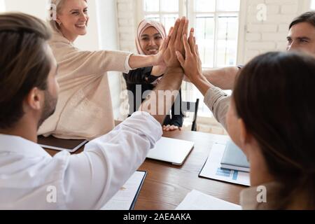 Happy mixed race young and older colleagues giving high five. Stock Photo