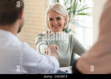 Head shot happy mature businesswoman shaking hands with partners. Stock Photo