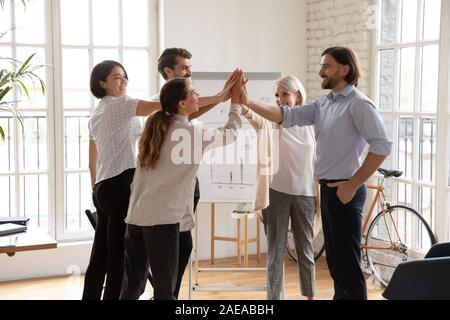 Overjoyed middle aged and young multiracial colleagues giving high five. Stock Photo