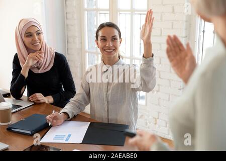 Smiling mixed race young female teammate raising hand. Stock Photo