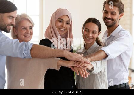 Happy mixed race young and older coworkers joining hands together. Stock Photo