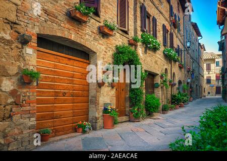 Majestic antique brick buildings with cozy flowery entrances in the old narrow street, fabulous small village, Pienza, Tuscany, Italy, Europe Stock Photo