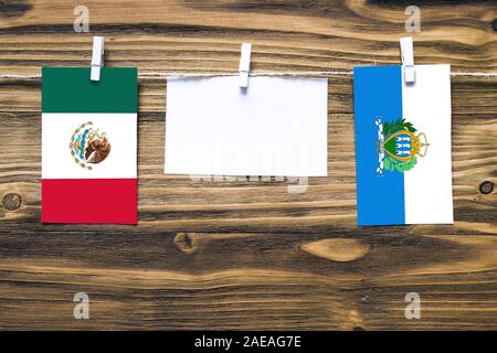 Hanging flags of Mexico and San Marino attached to rope with clothes pins with copy space on white note paper on wooden background.Diplomatic relation Stock Photo