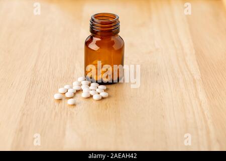 A set of white pills lying by a glass bottle of medicine on wooden table Stock Photo