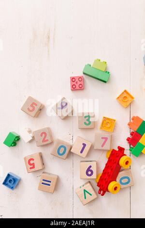 Top view on wooden cubes with numbers and colorful toy bricks on a white wooden background. Toys in the table. Stock Photo