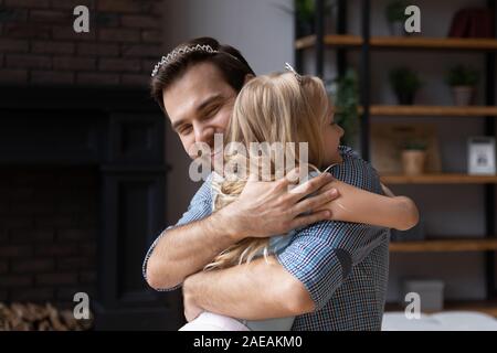 Father and adorable princess daughter wearing crowns hugging indoors Stock Photo