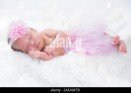 Cute newborn baby wears a pink flower crown lies swaddled in a white blanket. Stock Photo