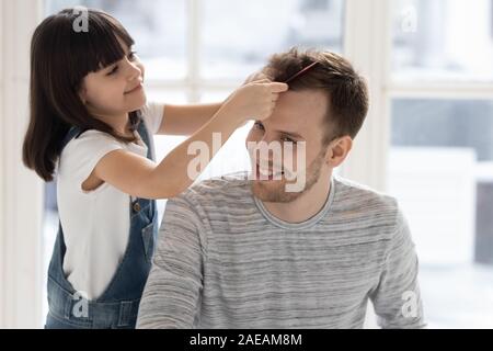 Caring happy preschool daughter brushing combing father hair. Stock Photo