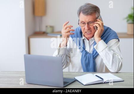 Discontented Elderly Man Calling To Customer Support Sitting At Workplace Stock Photo