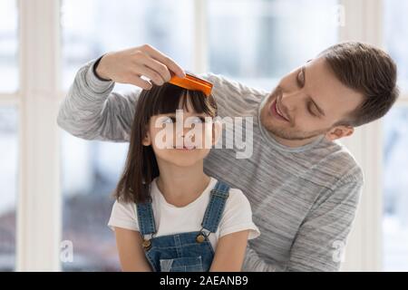 Caring happy father brushing combing preschool daughter hair. Stock Photo